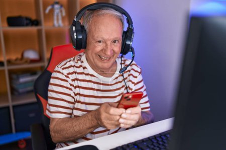 Téléchargez les photos : Homme aux cheveux gris moyen âge streamer à l'aide d'un ordinateur et smartphone à la salle de jeux - en image libre de droit