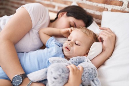 Téléchargez les photos : Mère et fils dormant sur le lit embrassant poupée dans la chambre - en image libre de droit