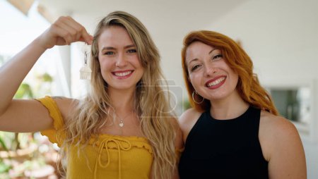 Téléchargez les photos : Deux femmes souriantes confiantes tenant la clé de la nouvelle maison à la maison terrasse - en image libre de droit