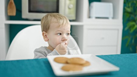 Photo for Caucasian toddler sitting on the table eating cookies at dinning room - Royalty Free Image