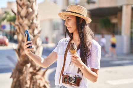 Foto de Joven turista hispana haciendo selfie junto al smartphone comiendo helado en la calle - Imagen libre de derechos