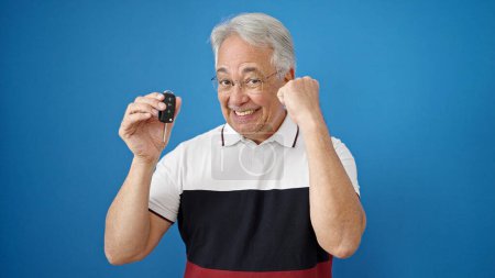 Photo for Middle age man with grey hair smiling confident holding key of new car celebrating over isolated blue background - Royalty Free Image