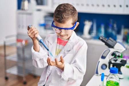 Foto de Niño rubio vistiendo uniforme científico usando pipeta en laboratorio - Imagen libre de derechos