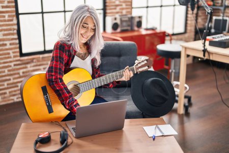 Photo for Middle age grey-haired woman musician playing classical guitar using laptop at music studio - Royalty Free Image