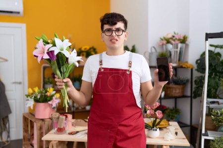 Photo for Young non binary man working at florist shop showing smartphone screen clueless and confused expression. doubt concept. - Royalty Free Image