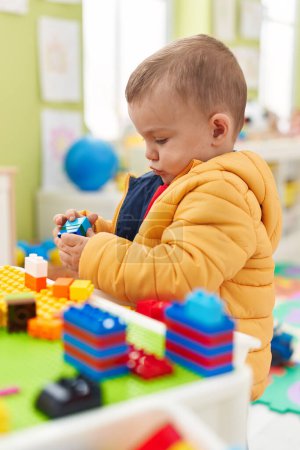 Foto de Adorable niño rubio jugando con bloques de construcción de pie en el jardín de infantes - Imagen libre de derechos