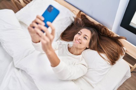 Foto de Mujer joven usando smartphone acostado en la cama en el dormitorio - Imagen libre de derechos