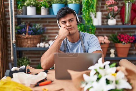 Photo for Hispanic young man working at florist shop doing video call serious face thinking about question with hand on chin, thoughtful about confusing idea - Royalty Free Image