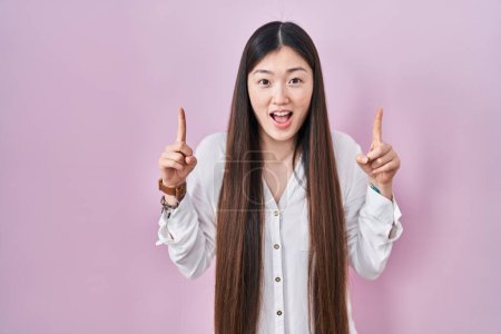 Téléchargez les photos : Chinois jeune femme debout sur fond rose souriant étonné et surpris et pointant vers le haut avec les doigts et les bras levés. - en image libre de droit