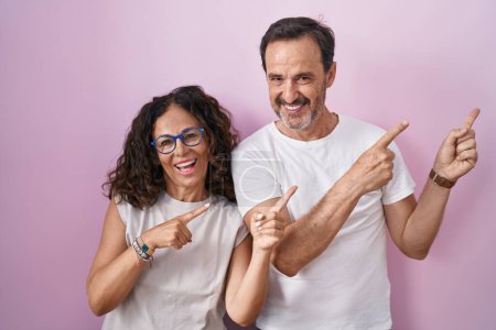 Photo for Middle age hispanic couple together over pink background smiling and looking at the camera pointing with two hands and fingers to the side. - Royalty Free Image