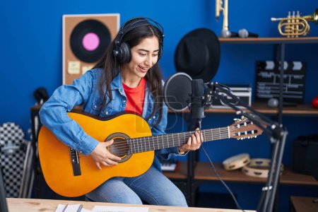 Foto de Joven chica hispana músico cantando canción tocando guitarra clásica en el estudio de música - Imagen libre de derechos