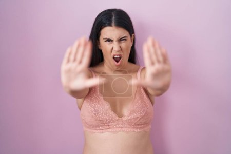 Téléchargez les photos : Jeune femme hispanique portant un soutien-gorge rose faisant geste d'arrêt avec les paumes des mains, expression de colère et de frustration - en image libre de droit