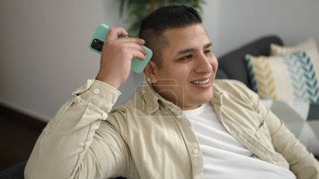 Foto de Joven hispano escuchando mensaje de voz con smartphone en casa - Imagen libre de derechos