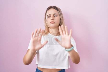 Photo for Young blonde woman standing over pink background moving away hands palms showing refusal and denial with afraid and disgusting expression. stop and forbidden. - Royalty Free Image
