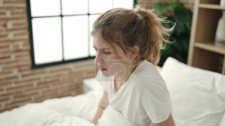 Foto de Mujer rubia joven estresada sentada en la cama en el dormitorio - Imagen libre de derechos