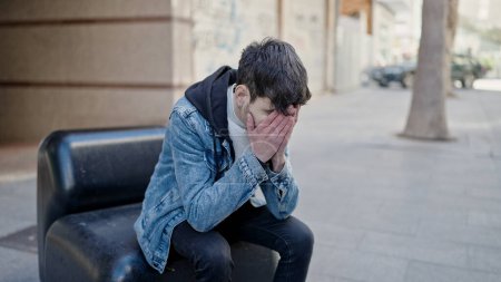 Foto de Joven hispano estresado sentado en un banco en la calle - Imagen libre de derechos