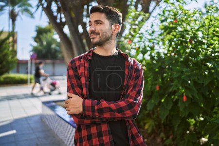 Téléchargez les photos : Jeune homme hispanique souriant confiant debout avec les bras croisés geste au parc - en image libre de droit