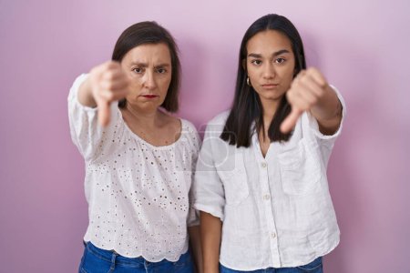 Foto de Madre e hija hispanas juntas se ven infelices y enojadas mostrando rechazo y negativo con el gesto de los pulgares hacia abajo. mala expresión. - Imagen libre de derechos