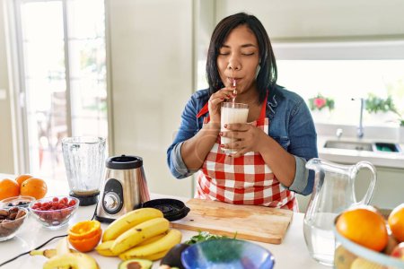 Foto de Hispanic brunette woman drinking fresh fruit smoothie at the kitchen - Imagen libre de derechos