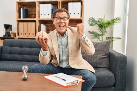Photo for Senior psychiatrist man working at consultation office celebrating victory with happy smile and winner expression with raised hands - Royalty Free Image