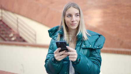 Photo for Young blonde woman using smartphone at street - Royalty Free Image