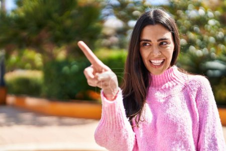 Foto de Joven mujer hispana sonriendo confiada señalando con el dedo al parque - Imagen libre de derechos