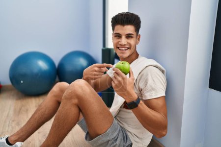 Téléchargez les photos : Jeune homme hispanique portant des vêtements de sport mangeant des pommes saines souriant heureux pointant avec la main et le doigt - en image libre de droit