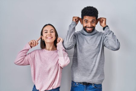 Photo for Young hispanic couple standing together smiling pulling ears with fingers, funny gesture. audition problem - Royalty Free Image