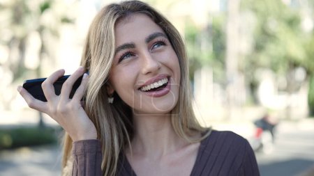 Foto de Mujer rubia joven sonriendo confiado escuchando mensaje de audio por el teléfono inteligente en el parque - Imagen libre de derechos
