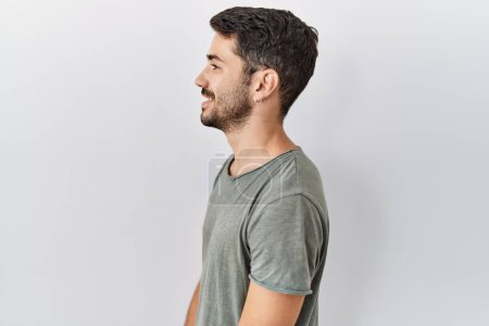 Photo for Young hispanic man with beard wearing casual t shirt over white background looking to side, relax profile pose with natural face with confident smile. - Royalty Free Image
