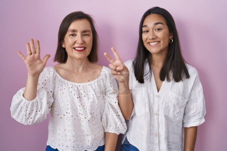 Foto de Madre e hija hispanas juntas mostrando y señalando con los dedos el número siete mientras sonríen confiadas y felices. - Imagen libre de derechos