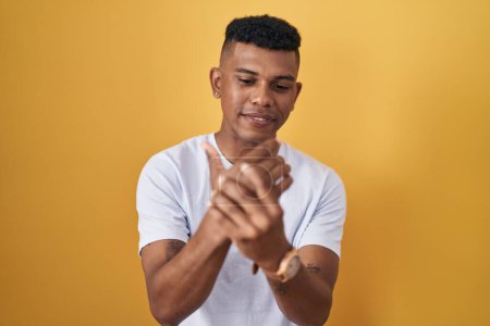 Photo for Young hispanic man standing over yellow background suffering pain on hands and fingers, arthritis inflammation - Royalty Free Image