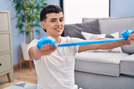 Téléchargez les photos : Young non binary man smiling confident using elastic band training at home - en image libre de droit