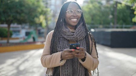 Téléchargez les photos : Femme africaine souriant à l'aide d'un smartphone au parc - en image libre de droit