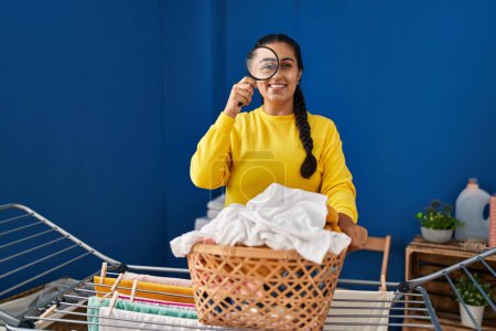 Photo for Young hispanic woman hanging clothes on clothesline using loupe at laundry room - Royalty Free Image