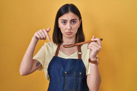 Photo for Hispanic girl eating healthy  wooden spoon pointing down looking sad and upset, indicating direction with fingers, unhappy and depressed. - Royalty Free Image