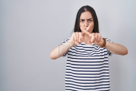 Foto de Mujer morena joven con rayas expresión rechazo camiseta cruzando los dedos haciendo signo negativo - Imagen libre de derechos