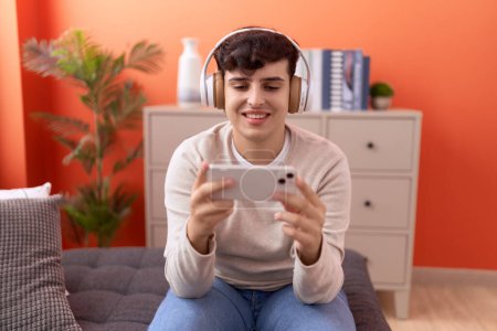 Téléchargez les photos : Homme non binaire souriant confiant jouer à un jeu vidéo à la maison - en image libre de droit