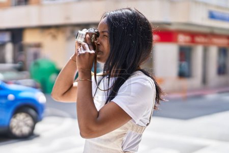 Téléchargez les photos : Jeune femme afro-américaine utilisant une caméra vintage à la rue - en image libre de droit