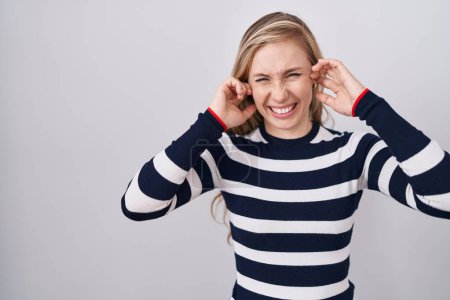 Foto de Mujer caucásica joven con suéter azul marino casual que cubre las orejas con los dedos con expresión molesta por el ruido de la música fuerte. concepto de sordo. - Imagen libre de derechos