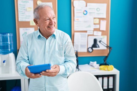 Foto de Trabajador de negocios hombre de pelo gris de mediana edad sonriendo confiado usando touchpad en la oficina - Imagen libre de derechos