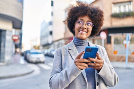 Téléchargez les photos : Afro-américaine femme exécutif souriant confiant en utilisant smartphone à la rue - en image libre de droit