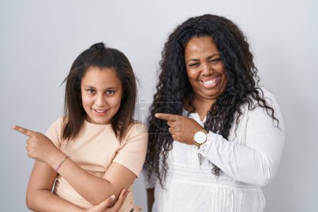 Photo for Mother and young daughter standing over white background with a big smile on face, pointing with hand finger to the side looking at the camera. - Royalty Free Image