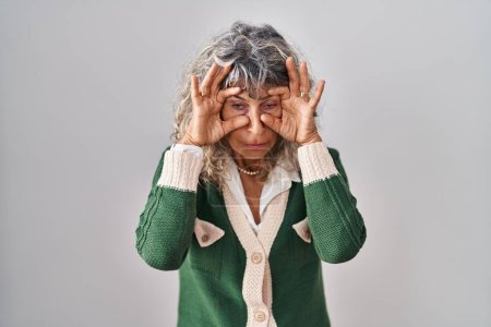Téléchargez les photos : Femme d'âge moyen debout sur fond blanc essayant d'ouvrir les yeux avec les doigts, somnolent et fatigué pour la fatigue matinale - en image libre de droit