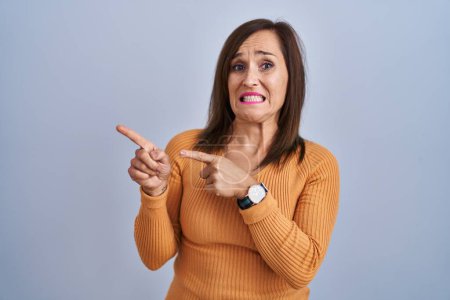 Téléchargez les photos : Femme brune du moyen âge debout portant un pull orange pointant de côté inquiet et nerveux avec les deux mains, préoccupé et expression surprise - en image libre de droit