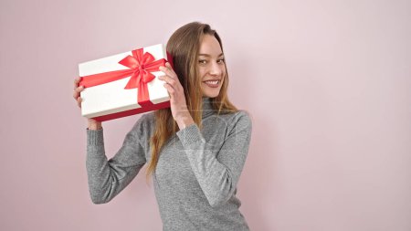 Photo for Young caucasian woman smiling confident hearing sound of birthday gift over isolated pink background - Royalty Free Image