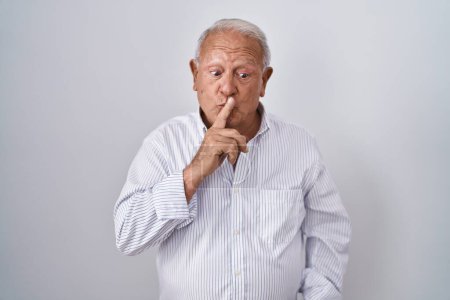 Téléchargez les photos : Homme âgé avec les cheveux gris debout sur fond isolé demandant à être calme avec le doigt sur les lèvres. silence et concept secret. - en image libre de droit