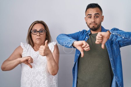Photo for Hispanic mother and son standing together doing thumbs up and down, disagreement and agreement expression. crazy conflict - Royalty Free Image