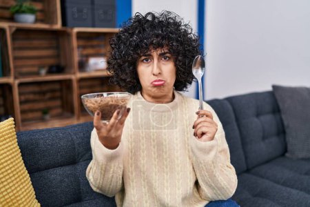 Photo for Young brunette woman with curly hair eating healthy whole grain cereals with spoon depressed and worry for distress, crying angry and afraid. sad expression. - Royalty Free Image
