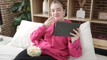 Photo for Young blonde woman watching movie sitting on bed at bedroom - Royalty Free Image